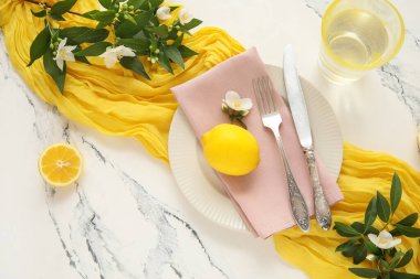 Çatal bıçak, peçete, limon ve yeşil dallarla mermer arka planda güzel bir masa.