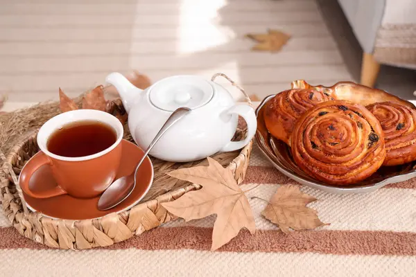 Bir fincan sıcak içecek, lezzetli çörekler ve sonbahar yapraklarıyla dolu bir çaydanlık.