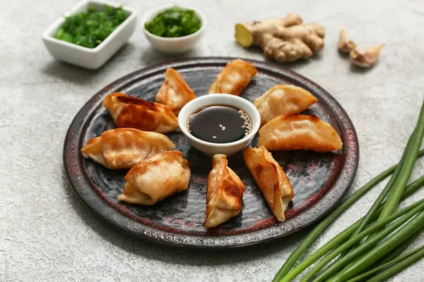Kızarmış Japon gyoza tabağı ve bir kase yosun salatası ve gri arka planda yeşil soğan.