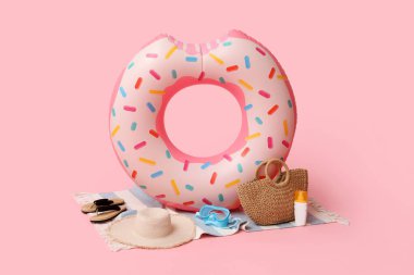 Donut şeklinde şişirilebilir yüzük, bir şişe güneş kremi ve pembe arka planda plaj aksesuarları, yakın plan.