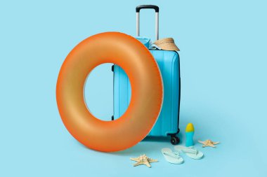 Mavi arka planda şişirilebilir yüzük, bavul ve plaj aksesuarları, yakın plan.