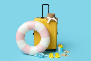 Şişirilebilir yüzük, bavul, güneş kremi şişeleri ve mavi arka planda plaj aksesuarları, yakın plan.