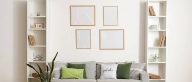 Yastıklı rahat kanepe, çiçek, kitap ve çerçeveli puf oturma odasında.