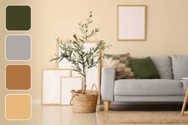 Modern oturma odasının içinde zeytin ağacı ve bej duvarın yanında boş çerçeveler var. Farklı renk desenleri