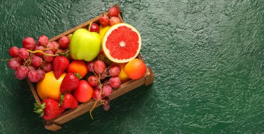 Tahta kutu ve yeşil masada farklı taze meyveler.