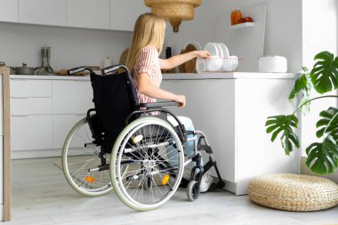 Tekerlekli sandalyedeki genç kadın evde yemek yiyor.