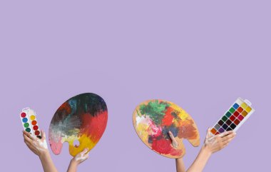 Suluboya boyalı kadın elleri ve leylak arka planda paletler.