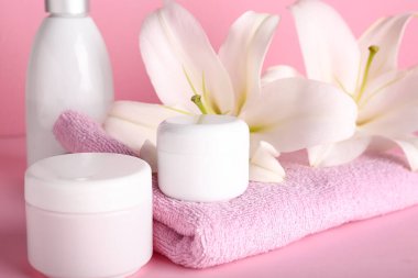 Kozmetik ürünler seti, temiz havlu ve pembe arka planda güzel zambak çiçekleri, yakın plan
