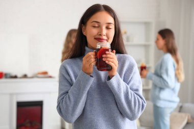 Partide oturma odasında elinde bir bardak sıcak şarapla genç ve güzel bir kadın.