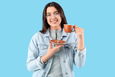 Mavi arka planda çay fincanı olan gözlüklü genç bayan.