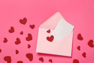 Zarflı kompozisyon, kart ve pembe arka planda kırmızı kalpler. Sevgililer Günü kutlaması