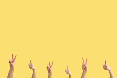 Sarı arka planda barış ve baş parmak hareketlerini gösteren kadın elleri