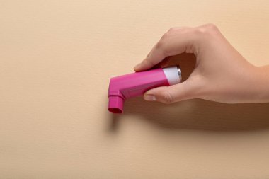 Bej arka planda astım spreyi olan bir çocuk eli.