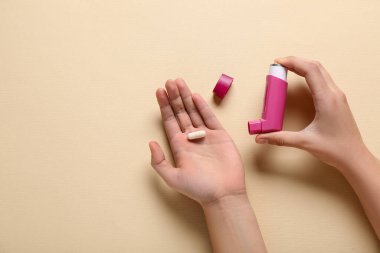 Astım spreyli çocuk elleri ve bej arka planda hap.