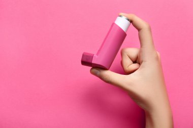 Pembe arka planda astım spreyi olan bir çocuk eli.