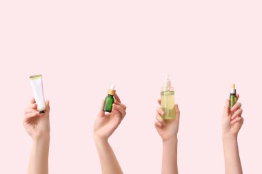 Pembe arka planda farklı kozmetik ürünleri olan kadın elleri