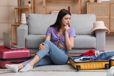 Oturma odasındaki kanepenin yanında bavulları olan düşünceli genç bir bayan.