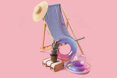Şişirilebilir halkalar, güverte sandalyesi ve pembe arka planda ananas ve güneş gözlüğü olan bavul. Seyahat kavramı