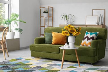 Oturma odasının içinde yeşil kanepe ve sehpanın üzerinde ayçiçekleri.