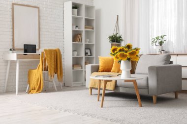 Oturma odasının içinde kanepe, işyeri ve sehpanın üzerinde ayçiçekleri var.