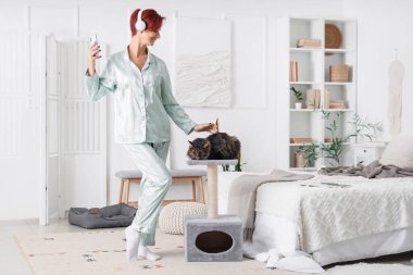 Güzel, mutlu, kulaklık takan, evde kedisi ve cep telefonu olan olgun bir kadın.