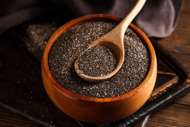 Ahşap arka planda chia tohumları olan kase ve kaşık, yakın plan.
