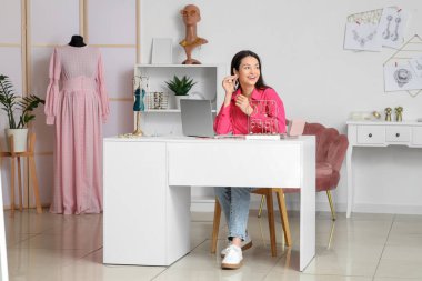 Atölyedeki masada küpe takan kadın mücevher tasarımcısı.