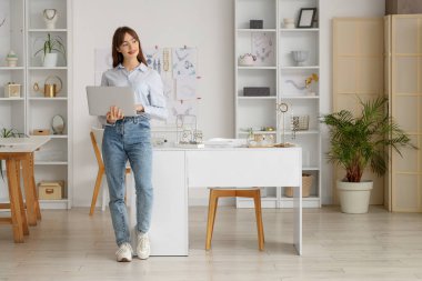 Genç bayan mücevher tasarımcısı atölyede dizüstü bilgisayarla çalışıyor.