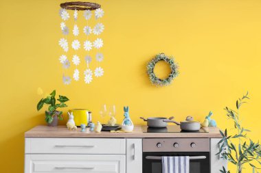 Fırın, çatal bıçak ve Paskalya süslemeleriyle dolu mutfak tezgahı sarı duvarın yanında.