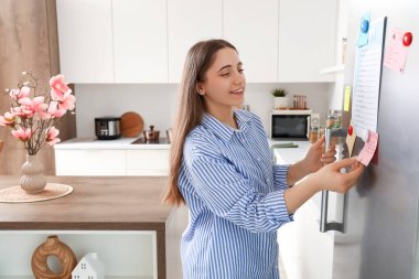 Mutfaktaki buzdolabında yapılacaklar listesi olan genç bir kadın.