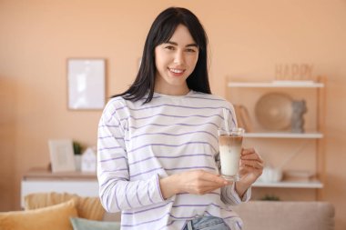Evde bir bardak buzlu latte içen genç bir kadın.