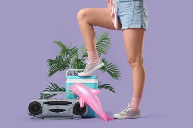 Portatif buzdolabı, retro müzik çalar ve eflatun arka planda şişme yunus olan genç bir kadın.