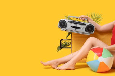 Bavullu genç kadın, retro müzik çalar ve sarı arka planda şişme top.