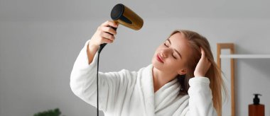 Saçlarını banyoda kurutan güzel bir genç kadın.