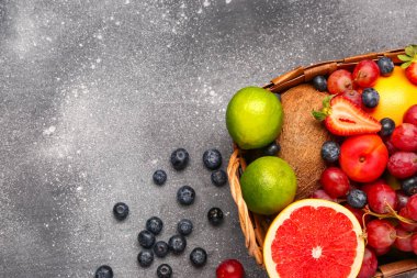 Gri masada farklı taze meyvelerle dolu sepet.
