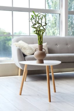 Pencerenin yanındaki masada yeşil bambu saplı vazo.