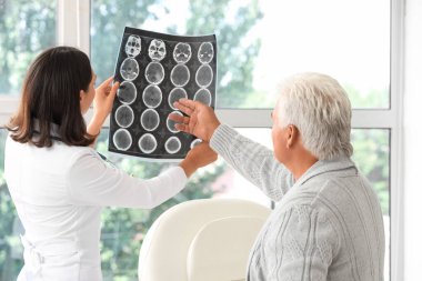 Kadın doktor muayenehanedeki yaşlı hastaya röntgen taraması gösteriyor.