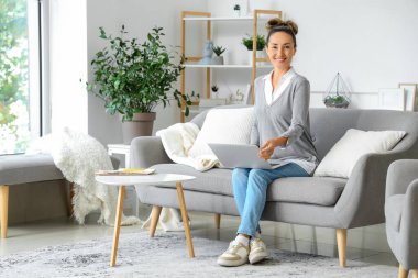 Evdeki kanepede dizüstü bilgisayarı olan olgun bir kadın.