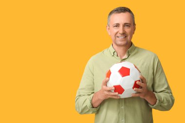 Sarı arka planda futbol topu olan yakışıklı olgun bir adam.