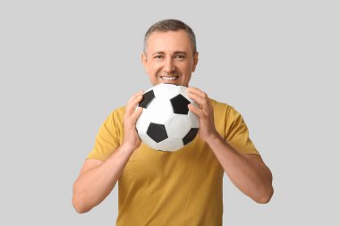 Gri arka planda futbol topuyla oynayan yakışıklı olgun bir adam.