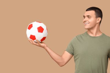 Kahverengi arka planda futbol topu olan yakışıklı bir genç.