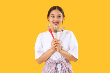 Sarı arka planda boya fırçası olan genç Asyalı kadın.