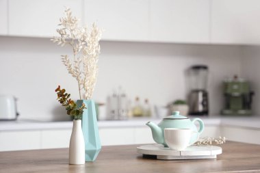 Çay takımlı ahşap masa, kurutulmuş çiçekler ve modern mutfakta okaliptüs dalları, yakın çekim.