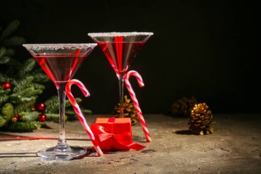 Bir bardak lezzetli kırmızı margarita, baston şekerler ve karanlık arka planda Noel dekoru.