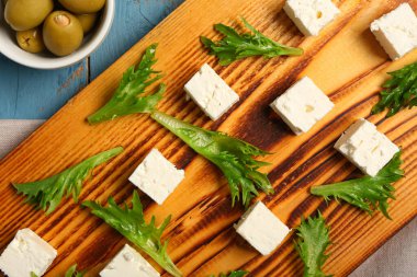 Mavi ahşap arka planda beyaz peynir, marul ve bir kase zeytin, yakın plan.