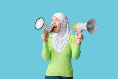 Genç Asyalı Müslüman kadın mavi arka planda megafonlara bağırıyor. Ulusal Duyulma Günü