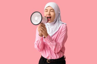 Genç Asyalı Müslüman kadın pembe arka planda megafona bağırıyor. Ulusal Duyulma Günü