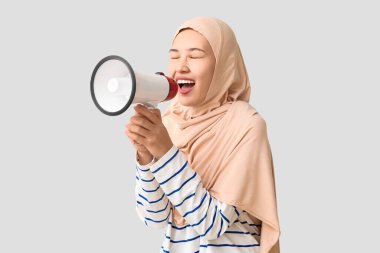 Genç Asyalı Müslüman kadın gri arka planda megafona bağırıyor. Ulusal Duyulma Günü