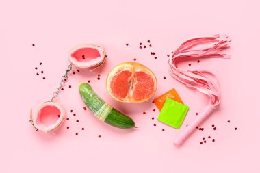 Seks oyuncaklı prezervatifler, pembe arka planda taze greyfurt ve salatalık. Seks eğitimi