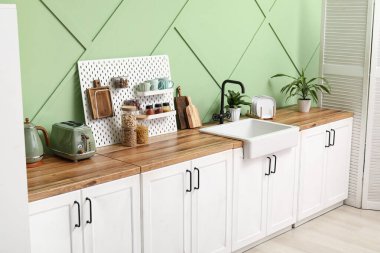 Beyaz tezgahlı, tahta tahtalı ve yeşil duvarlı şık bir mutfak.